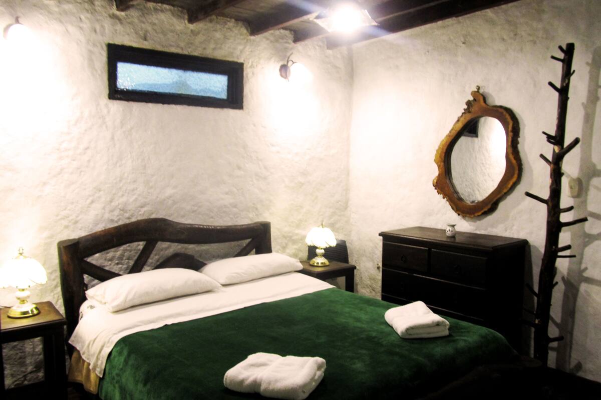 A bedroom with a bed, a nightstand, a dresser, a mirror, and a coat rack.