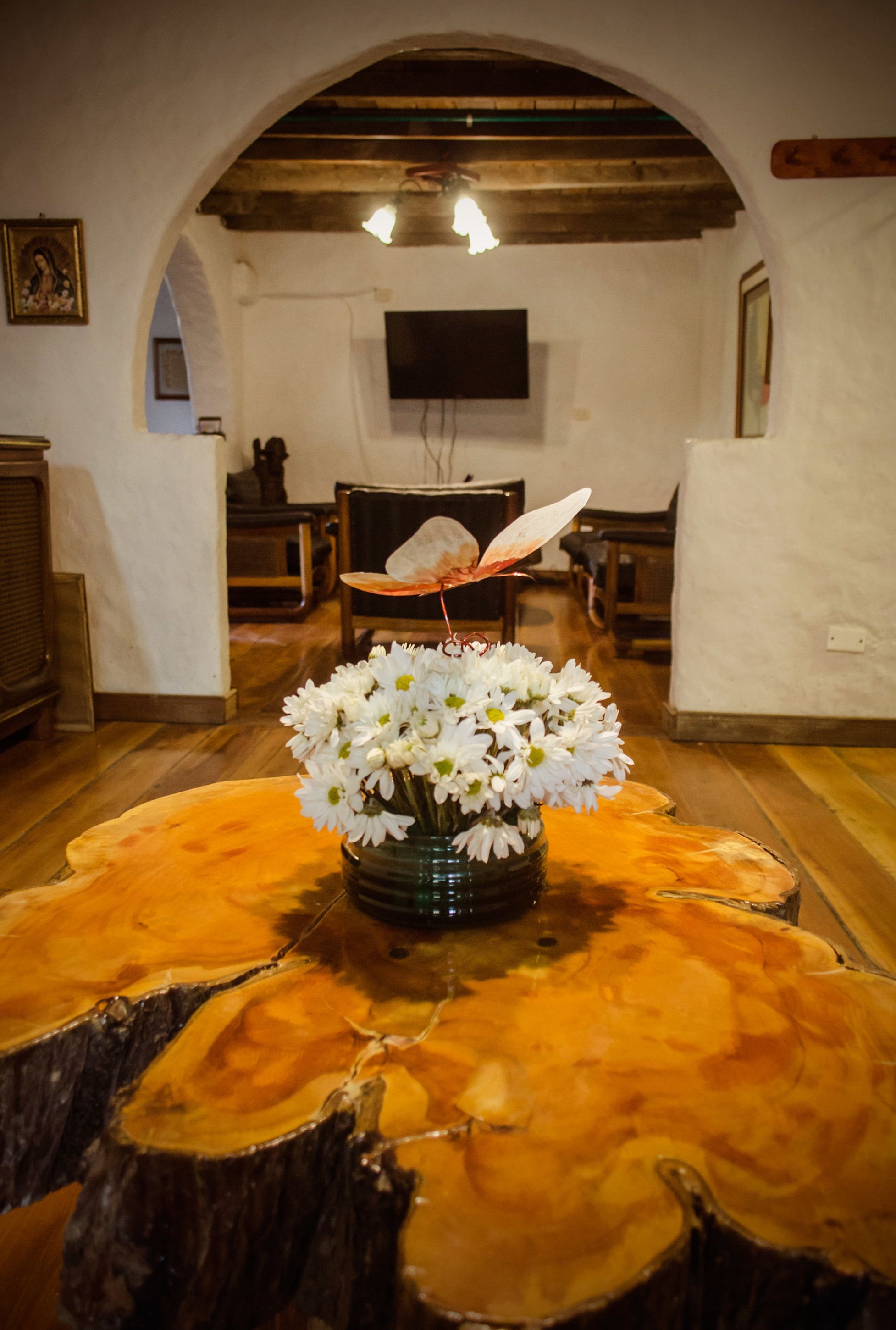 A room with a wooden table, a vase of white flowers, and a television on the wall.