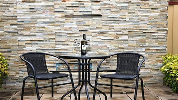 A patio area with a stone wall, two black metal chairs, and a table with a bottle. - City Mews (GOWANBRAE)