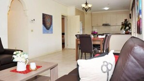 A living room with a sofa, a coffee table with a vase and a candle, a dining area with a table and chairs, and a kitchen in the background. - City Mews (GOWANBRAE)