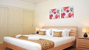 A neatly made bed with a wooden frame, white bedding, and decorative pillows. There are two wall-mounted paintings of flowers. - City Mews (GOWANBRAE)