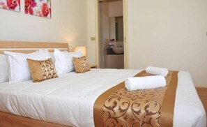 Ein ordentlich bezogenes Bett mit weißer und brauner Bettwäsche, einem Kopfteil und einer dekorativen Gold-Muster-Decke.
