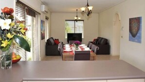 A dining area with a table set for four, two sofas, a TV, and a painting on the wall. - City Mews (GOWANBRAE)