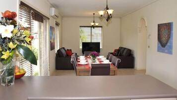 A dining area with a table set for four, two sofas, a TV, and a painting on the wall.