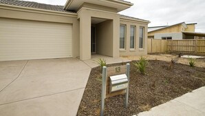 A modern single-story house with a garage, a small front yard with mulch and plants, and a mailbox with the number 13. - Villa Jemma (POINT COOK)
