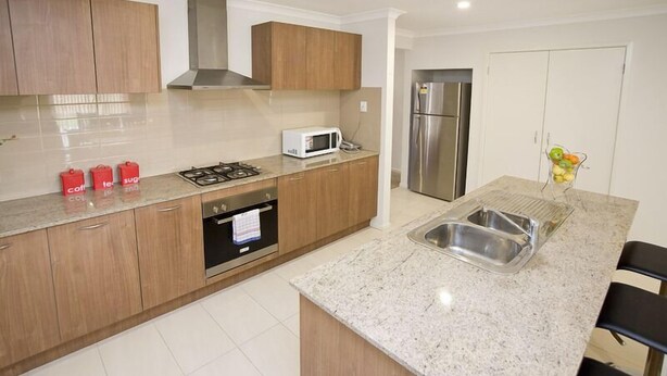 A modern kitchen with wooden cabinets, a gas stove, a microwave, and a stainless steel refrigerator. - Villa Jemma (POINT COOK)