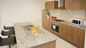 A modern kitchen with a granite countertop, stainless steel appliances, wooden cabinets, and a built-in oven. - Villa Jemma (POINT COOK)