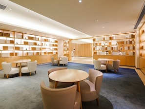A modern library with round tables and chairs, wooden bookshelves, and a blue carpet. - JI Hotel Guangzhou Tianhe East Railway Station (Guangzhou)