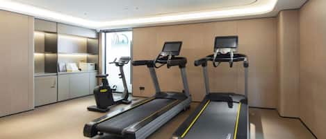 A modern gym with three treadmills, a stationary bike, and a weight bench.