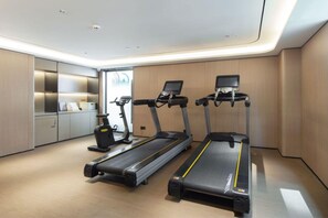 Une salle de sport moderne équipée de trois tapis de course, d’un vélo d’appartement et d’un banc de musculation.
