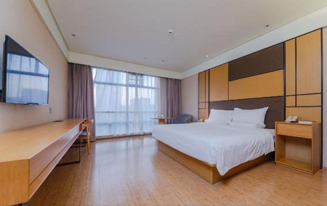 A modern hotel room with a large bed, a desk, a chair, and a TV mounted on the wall.