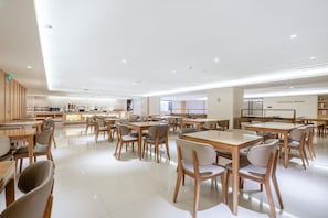 A modern dining area with wooden tables and chairs, a kitchen in the background, and a clean, white interior. - JI Hotel Guangzhou Tianhe East Railway Station (Guangzhou)