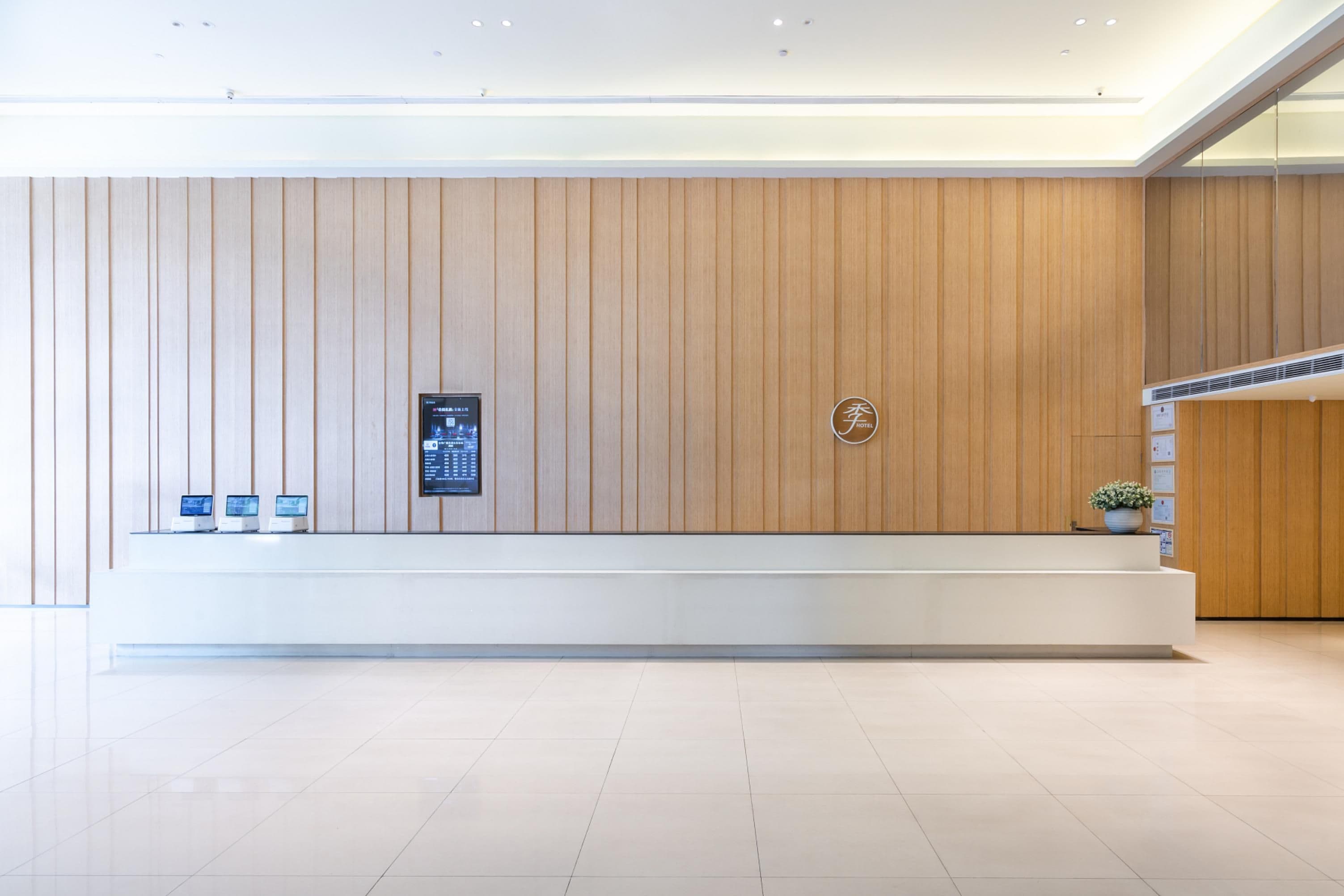 A modern reception area with a wooden panel wall, a reception desk, and a digital information board.
