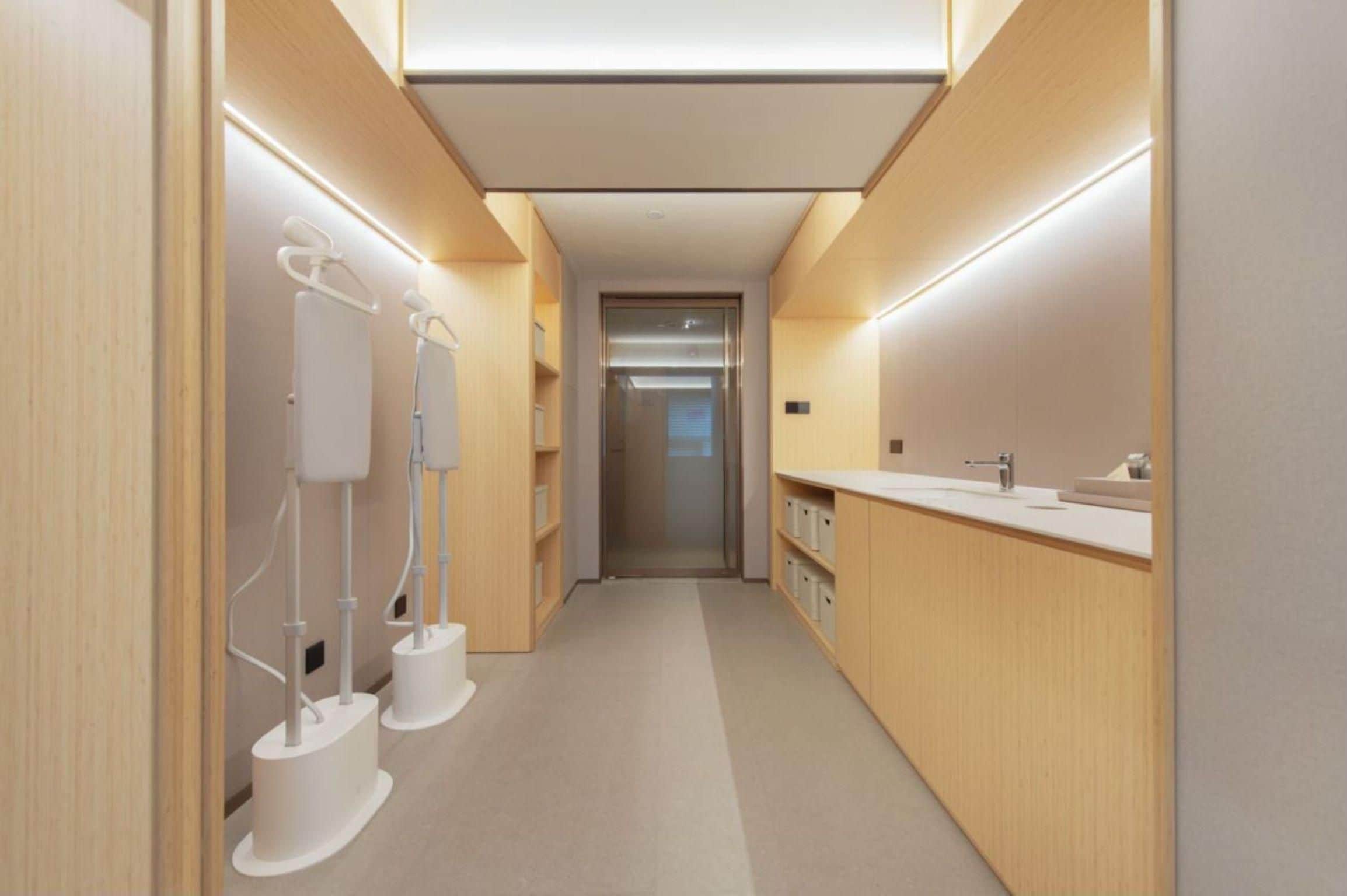A modern, well-lit hallway with wooden paneling, a central elevator, and a sink area on the right.