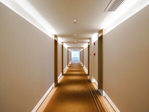 Un couloir d'hôtel avec un sol recouvert de moquette, des portes de chaque côté et une source de lumière au bout du couloir.