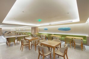 Un restaurant moderne au design épuré et minimaliste, avec des tables et des chaises en bois, un espace détente agrémenté de plantes et un intérieur lumineux et bien éclairé.