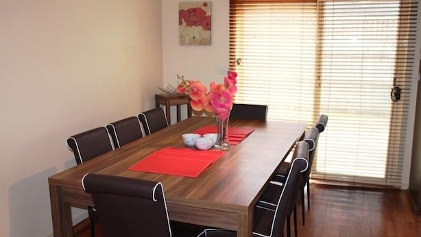 Een eetruimte met een houten tafel, zwarte stoelen en een vaas met roze bloemen.
