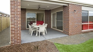 A covered patio area with a table and chairs, a red sofa, and a sliding glass door leading to a red room. - Villa Mystic (POINT COOK)