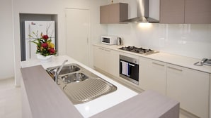 A modern kitchen with a stainless steel sink, a microwave, a gas stove, and a built-in oven. - Villa Mystic (POINT COOK)