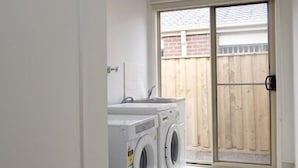 A laundry room with two washing machines and a sliding glass door leading to a backyard. - Villa Mystic (POINT COOK)