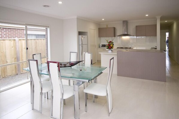 A modern kitchen with a central island, white cabinetry, and a glass dining table with white chairs.