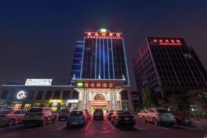 A hotel with a prominent entrance, multiple parking spaces, and adjacent taller buildings. - Vienna Hotel (Shanghai Sheshan Happy Valley) (Shanghai)