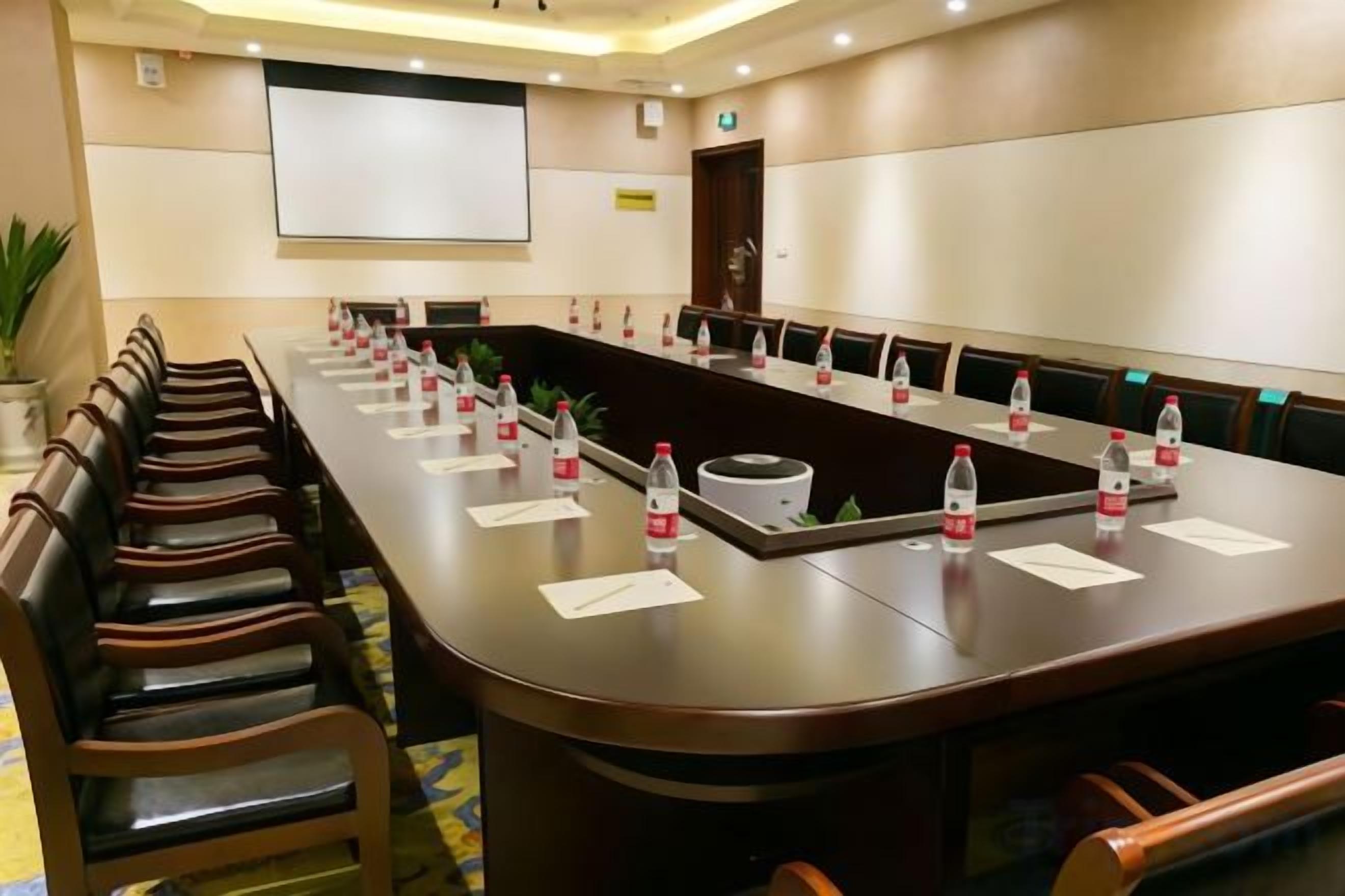 A conference room with a long table, chairs, water bottles, and a projector screen.