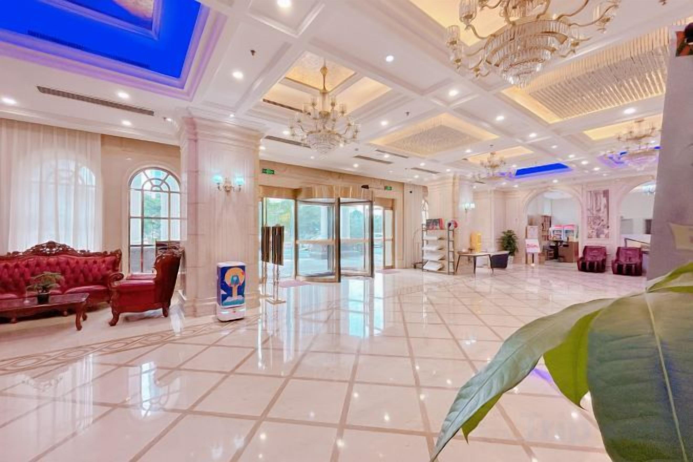 A spacious lobby with a marble floor, a red sofa, and a chandelier.