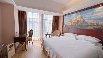 A hotel room with a large bed, a desk, a chair, a small table, and a painting of a cityscape.