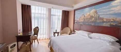 Habitación de hotel con una cama grande, un escritorio, una silla, una mesita y un cuadro de un paisaje urbano.