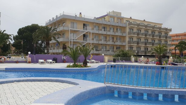 Un espace piscine avec une terrasse carrelée, des chaises longues et un bâtiment doté de balcons en arrière-plan.