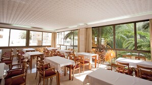 Un espace repas avec des tables et des chaises, de grandes fenêtres offrant une vue sur les palmiers.