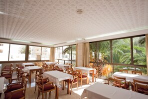 A dining area with tables and chairs, large windows with a view of palm trees. - Hostal BEI Juan Mallorca (Sant Llorenc des Cardassar)