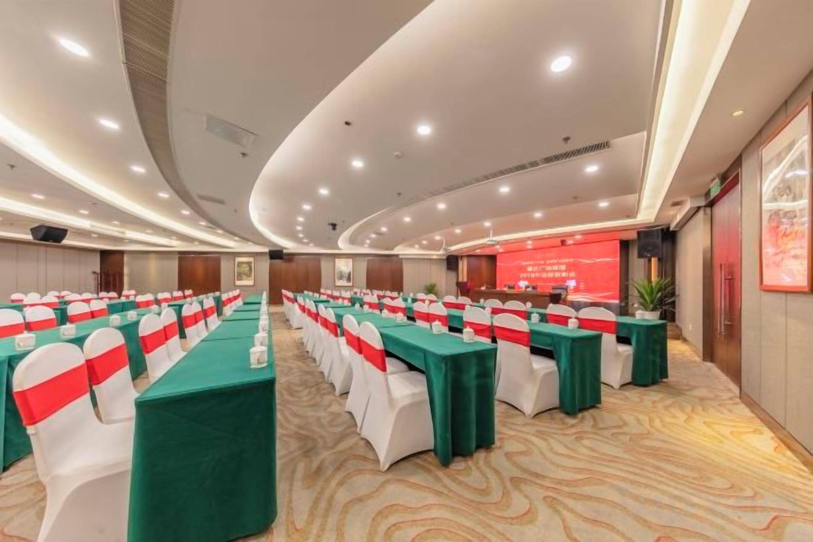 A conference room with rows of tables, each with a green tablecloth and white chairs, and a red banner on the wall.
