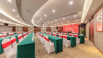A conference room with rows of tables, each with a green tablecloth and white chairs, and a red banner on the wall.
