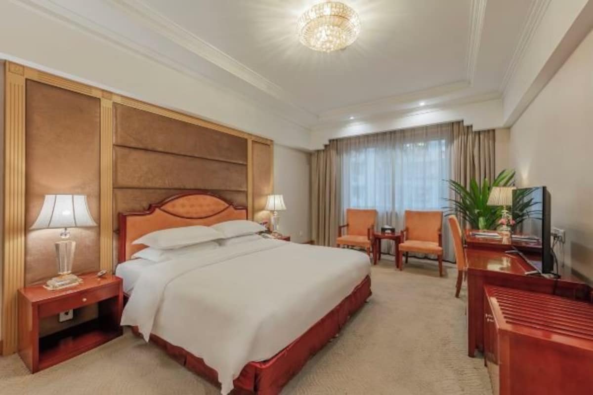 Une chambre d’hôtel avec un grand lit, deux tables de chevet avec des lampes, un bureau avec une chaise et un téléviseur.