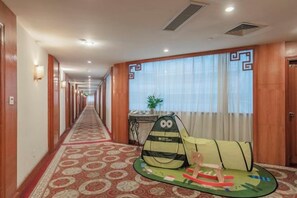 Un couloir d’hôtel avec un sol recouvert de moquette, un comptoir de réception et une fenêtre avec des rideaux.