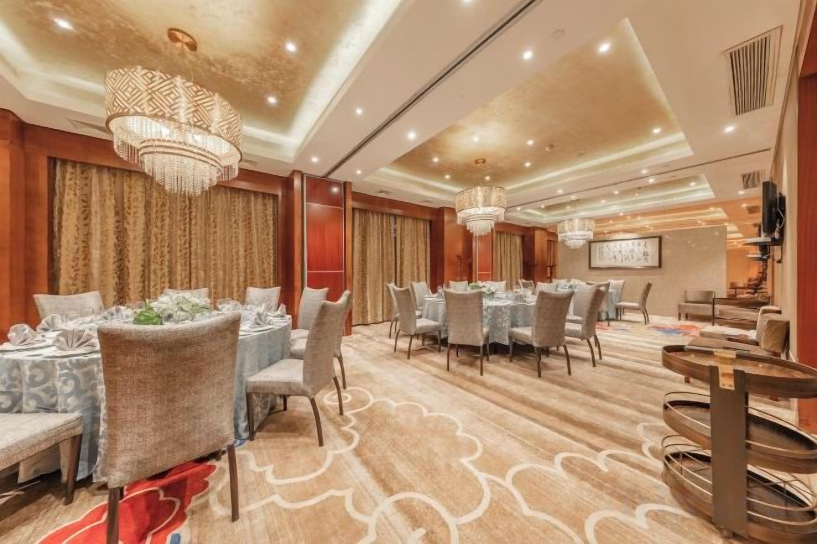 Uma sala de jantar de hotel com mesas redondas, cadeiras e lustres.