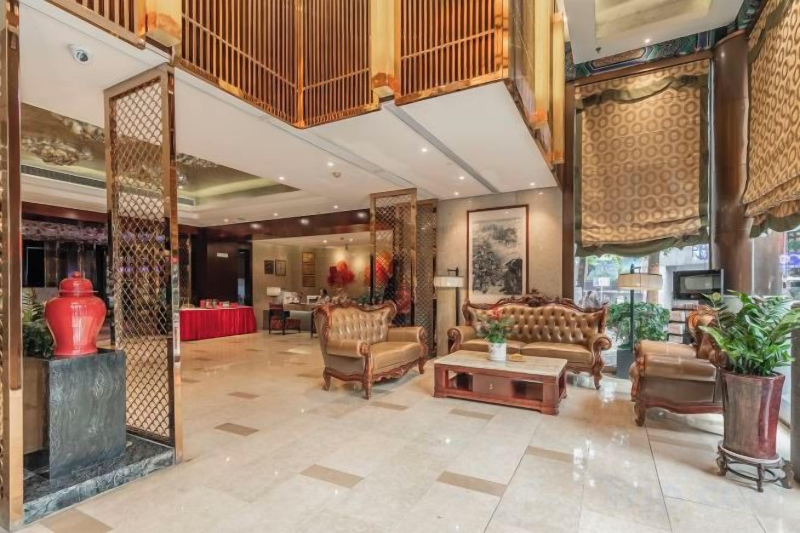 A spacious lobby with a high ceiling, traditional wooden furniture, and a red vase centerpiece.