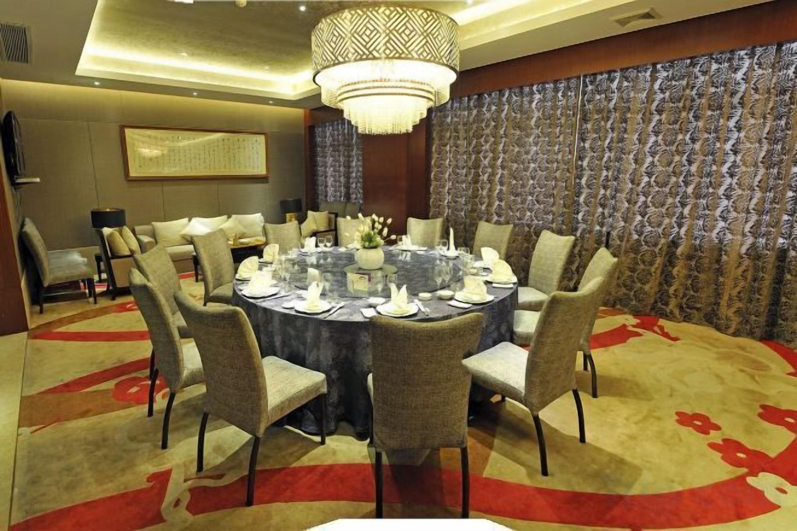 A round dining table with chairs, a chandelier, and a patterned wall in a hotel room.