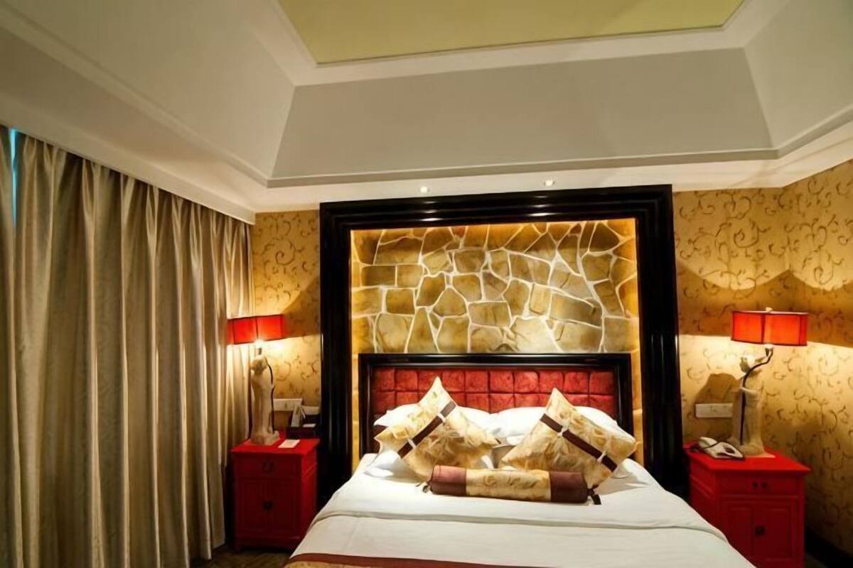Une chambre d’hôtel avec une tête de lit à motifs de pierre, un lit avec de nombreux oreillers, des tables de chevet rouges et des lampes.