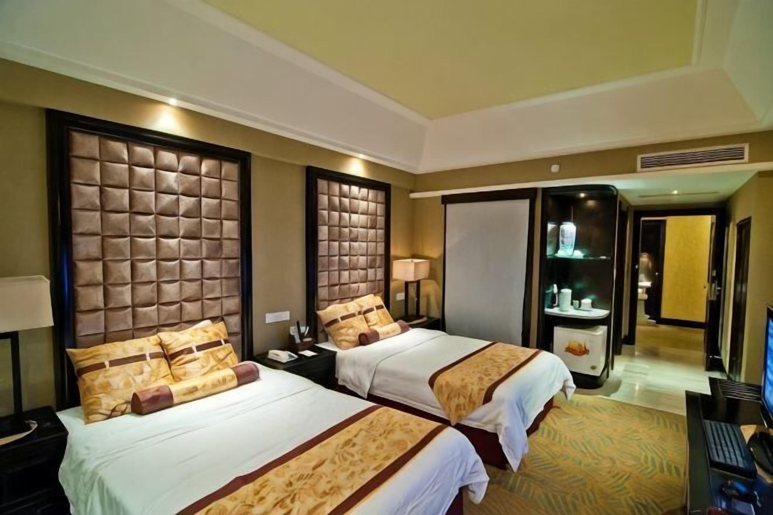 A hotel room with two beds, a desk, a computer, and a bathroom visible through an open door.