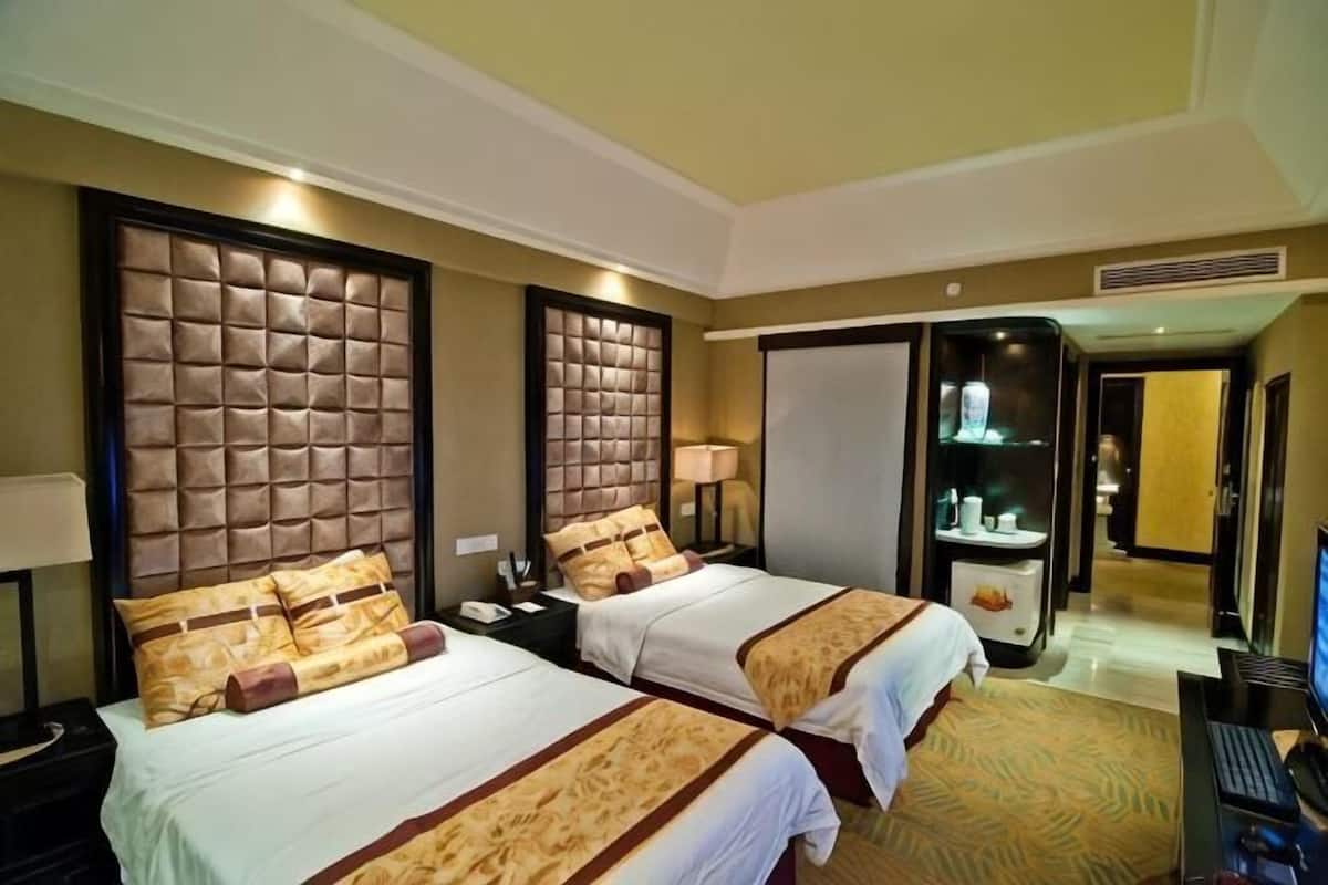 Une chambre d’hôtel avec deux lits, un bureau, un ordinateur et une salle de bain visible à travers une porte ouverte.