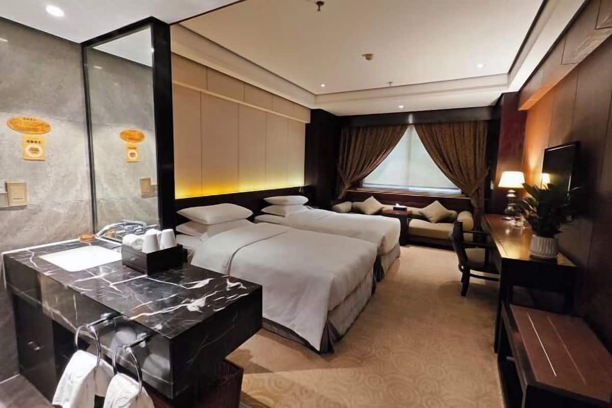 Une chambre d’hôtel avec une salle de bain en marbre, un lit avec du linge de maison blanc, un bureau et une télévision.