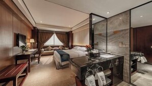 A hotel room with a bed, a desk, a chair, a large mirror, and a bathroom with a sink and towel rack.