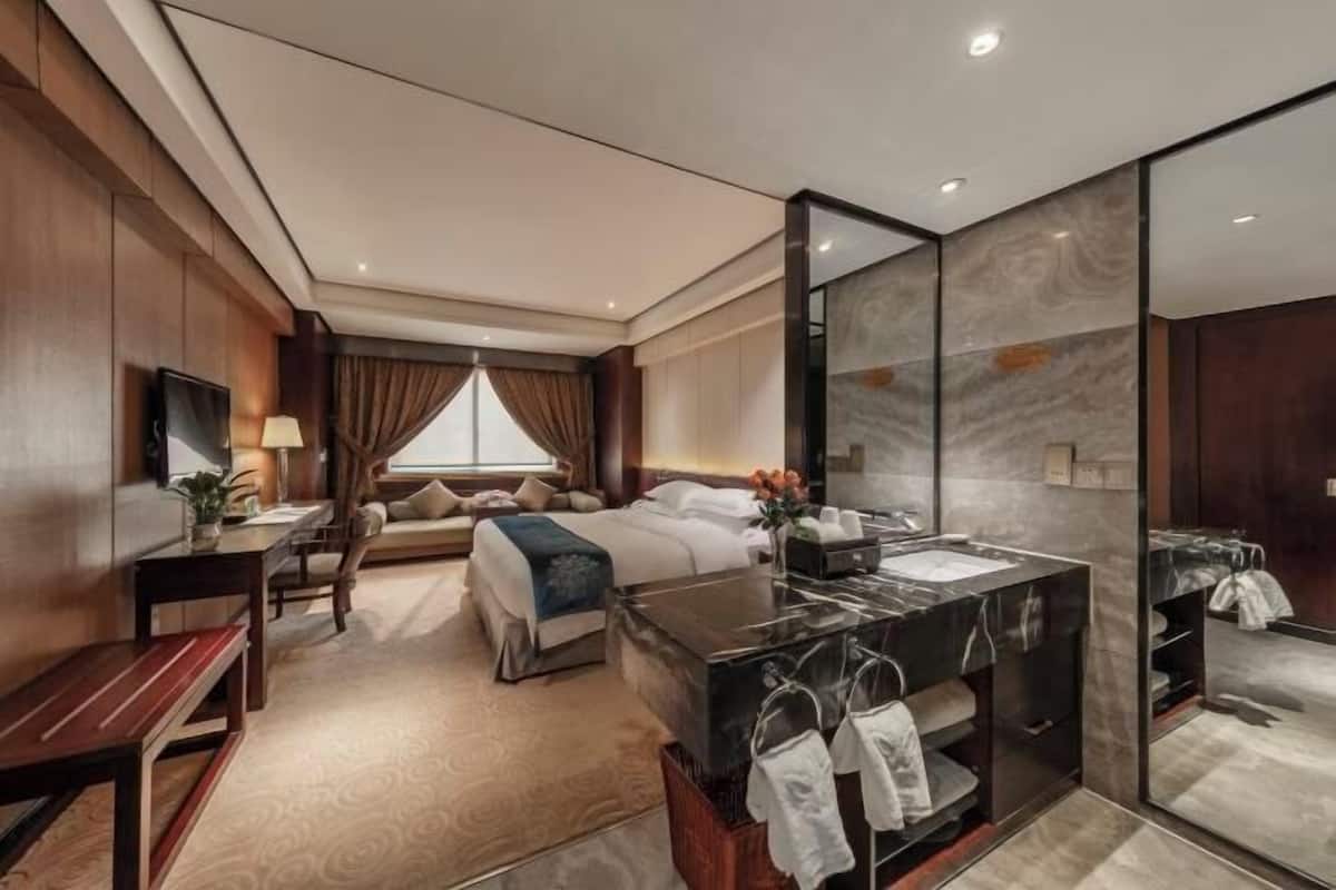 Une chambre d’hôtel comprenant un lit, un bureau, une chaise, un grand miroir et une salle de bain avec un lavabo et un porte-serviettes.