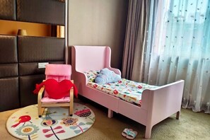 Een kinderkamer met een roze bed, een stoel met een hartvormig kussen en een kleurrijk vloerkleed.