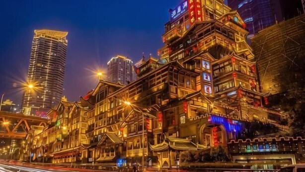 A traditional building with multiple stories, illuminated by artificial lighting, and surrounded by modern high-rise buildings.