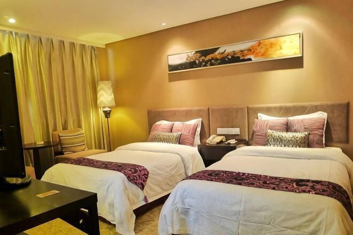 Une chambre d’hôtel avec deux lits, un bureau, une lampe et un tableau au mur.