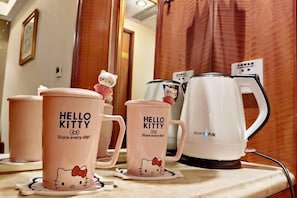 Une chambre d’hôtel avec un miroir dans lequel se reflètent une tasse à l’effigie de Hello Kitty, une autre tasse, plus petite, également à l’effigie de Hello Kitty, et une bouilloire électrique blanche posée sur le comptoir.